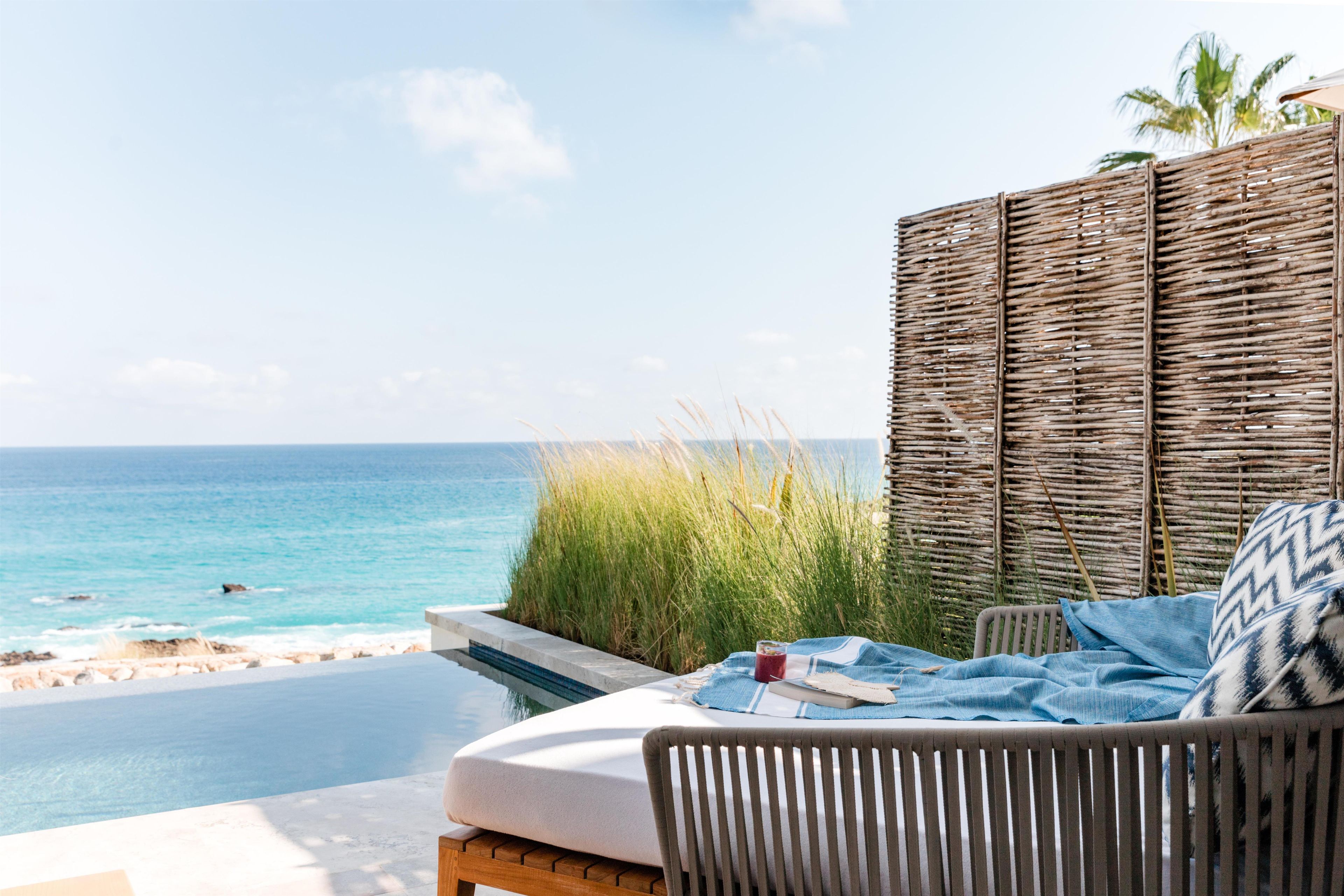 A seaside view with a wicker chair and a table with a drink, overlooking the ocean.