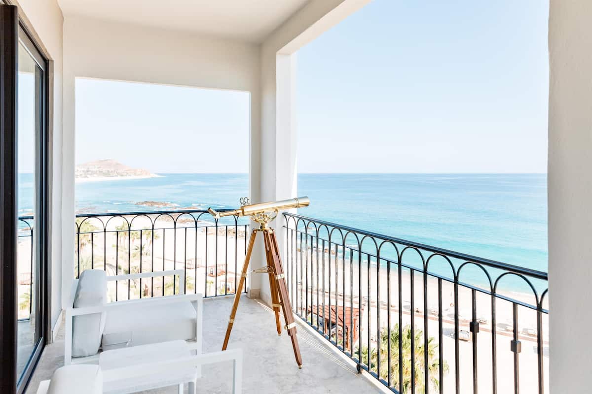 A balcony with a telescope, white furniture, and a view of the sea.
