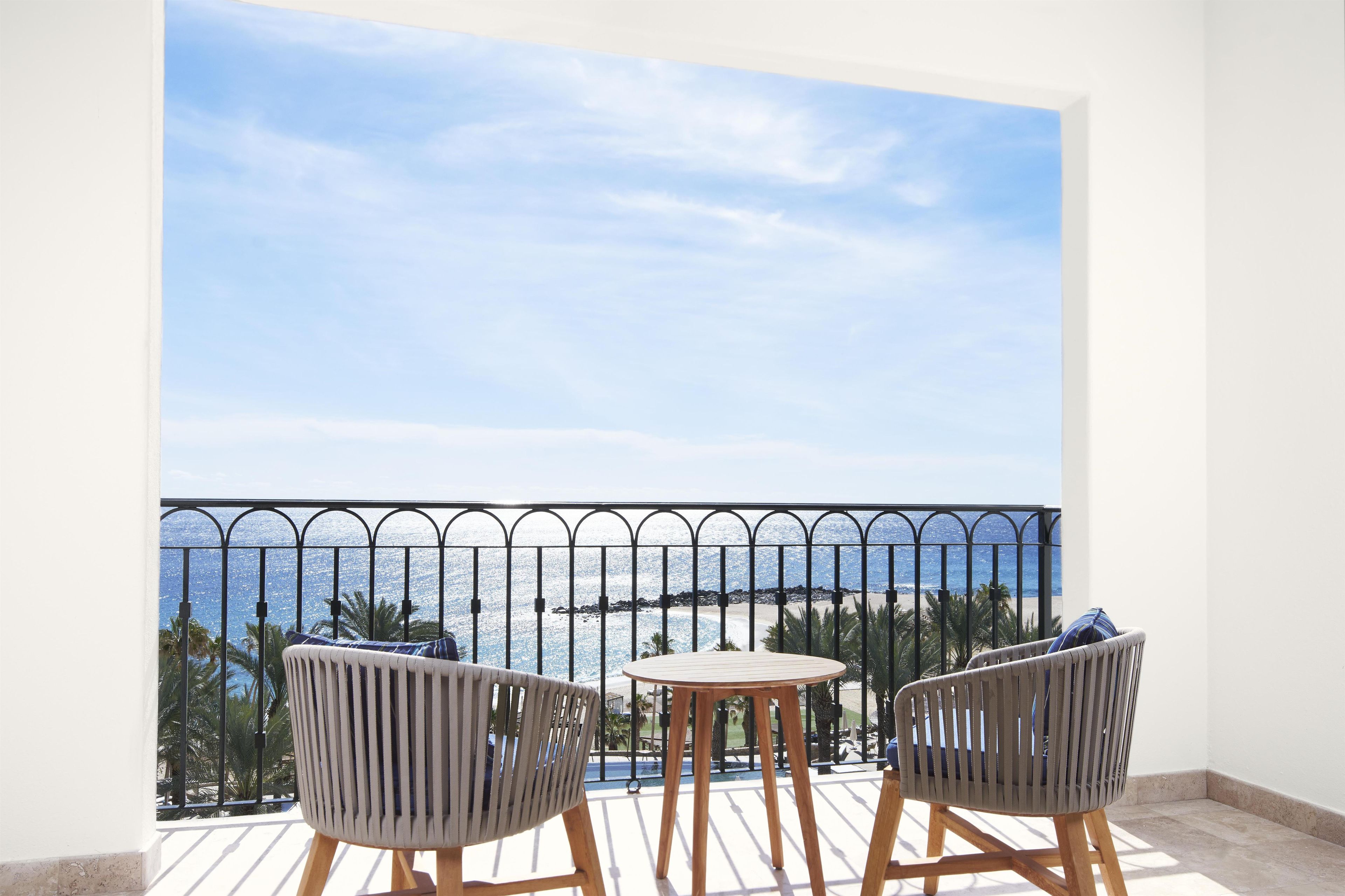 A balcony with two chairs and a table, overlooking a beach and the sea.