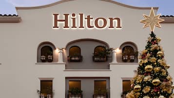 A building with the name 'Hilton' illuminated on the facade, balconies with potted plants, and a Christmas tree with ornaments.