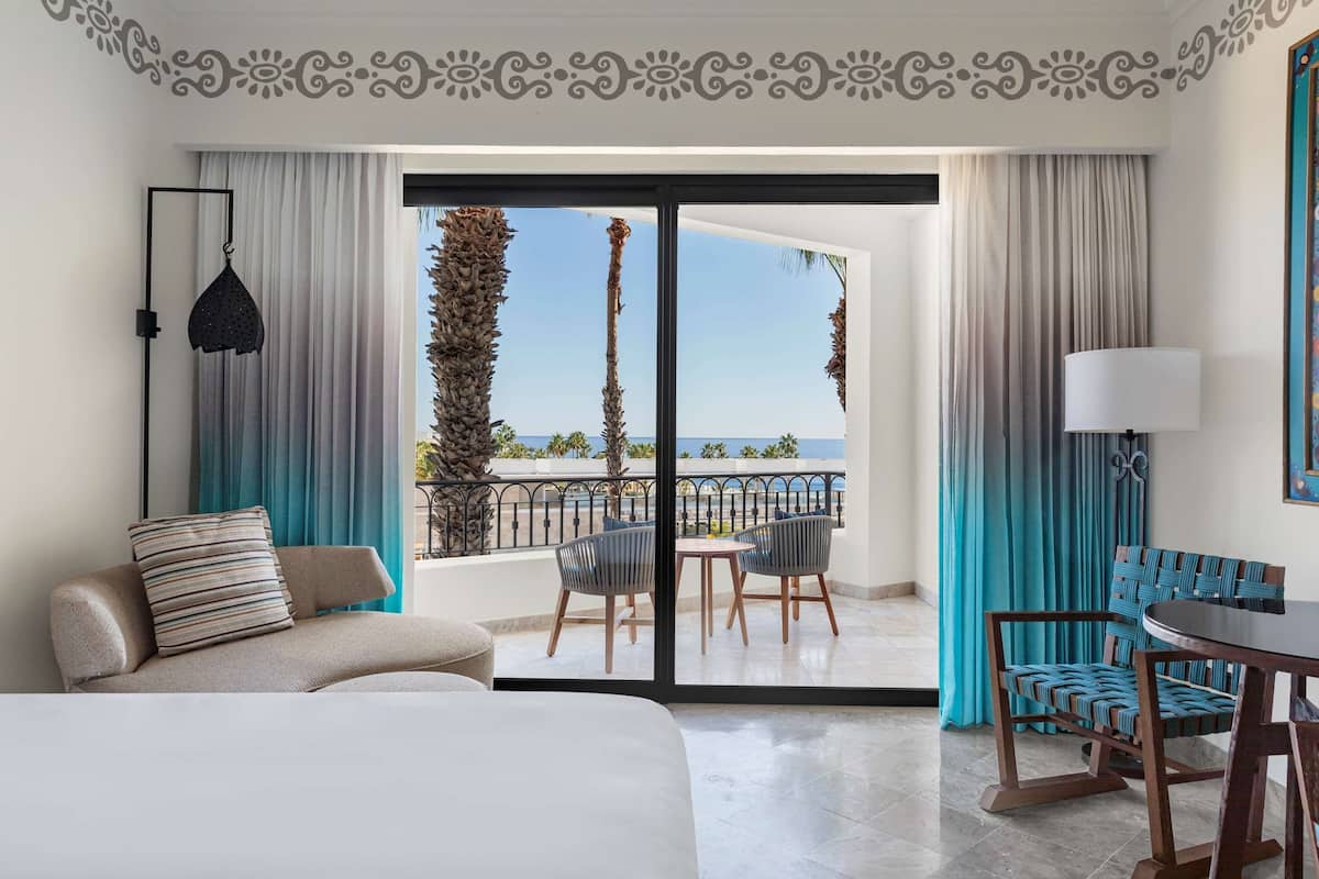 A hotel room with a balcony, a sofa, a dining table, and chairs.