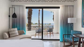A hotel room with a balcony, a sofa, a dining table, and chairs.