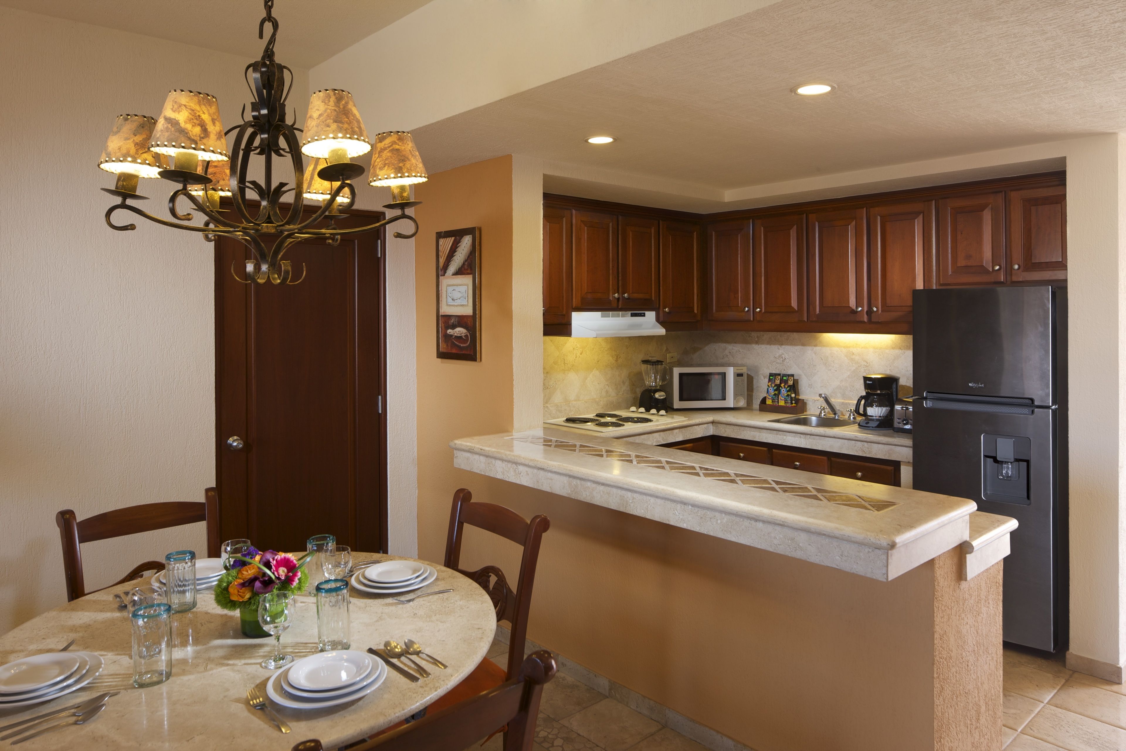 A kitchen with wooden cabinets, a black refrigerator, a microwave, and a dining area with a table set for four.