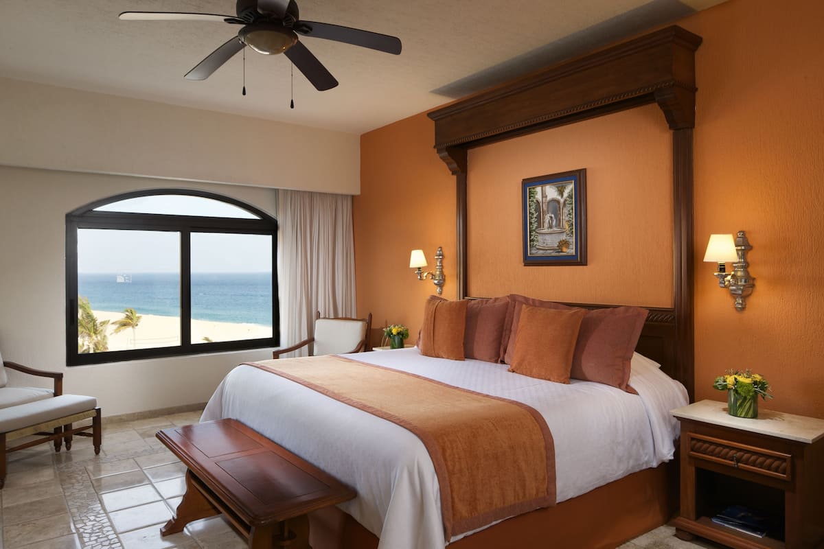 Une chambre d’hôtel avec un grand lit, un ventilateur de plafond, une vue sur la plage et une table de chevet avec une lampe.