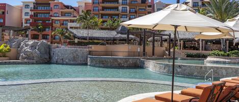 A resort pool area with lounge chairs and umbrellas, surrounded by a stone wall and palm trees.