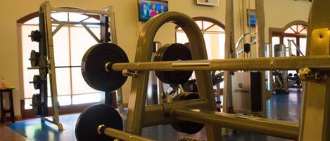 A gym with weightlifting equipment, a television on the wall, and a large window.