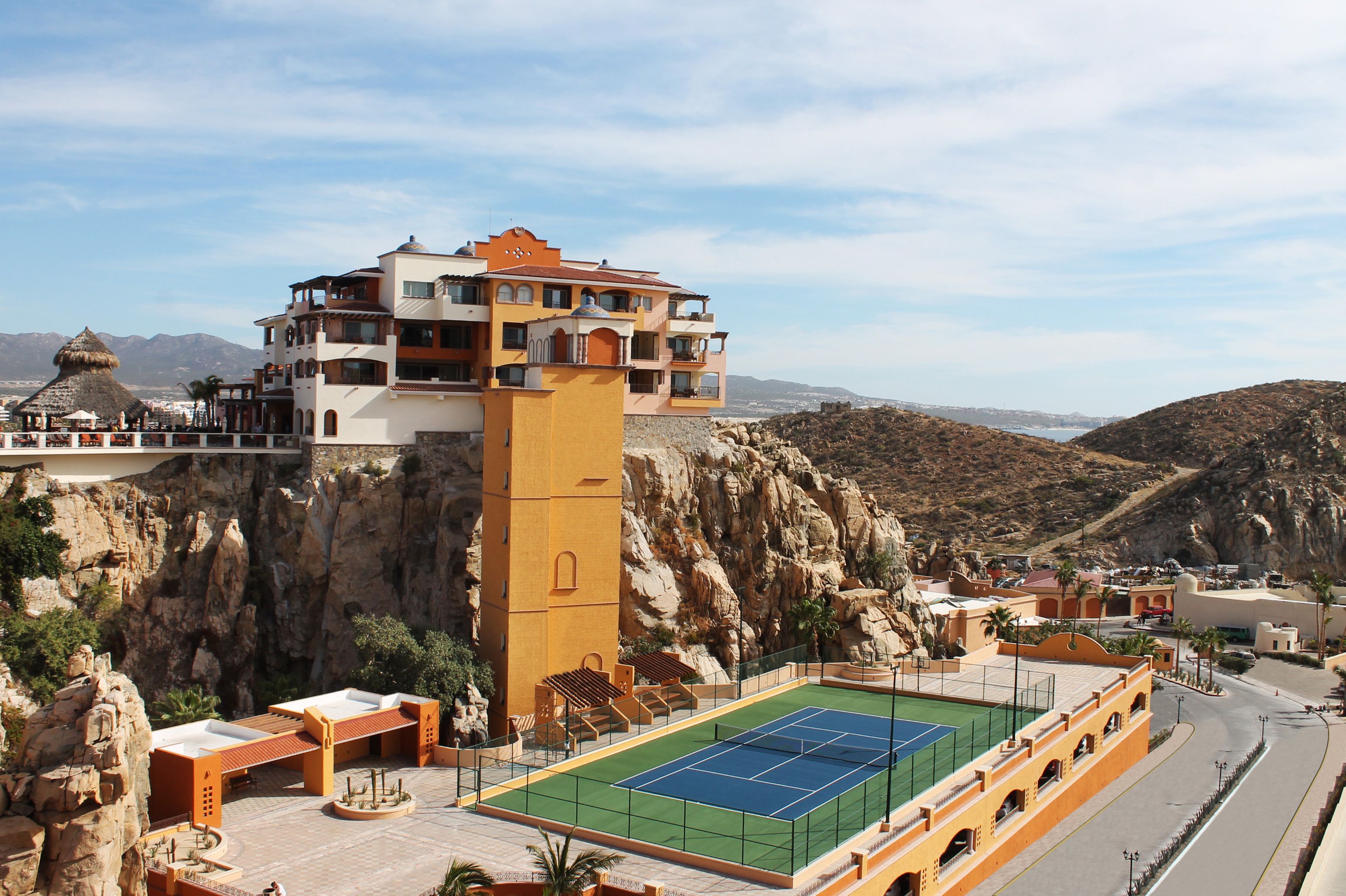 A high-rise hotel with a tennis court, located in a mountainous area with rocky terrain.