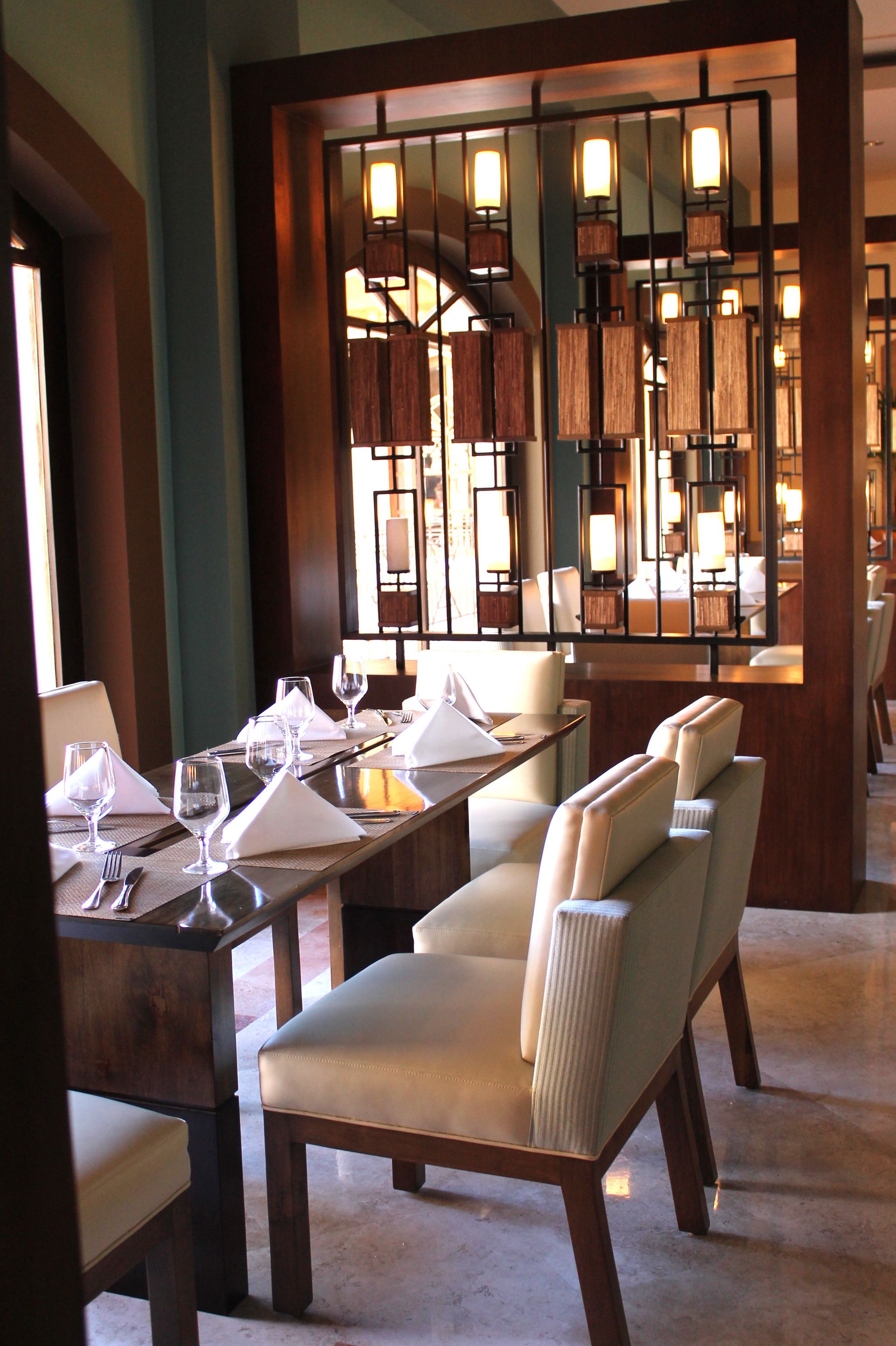 A dining area with a long table set for a meal, upholstered chairs, and a decorative partition with lights.