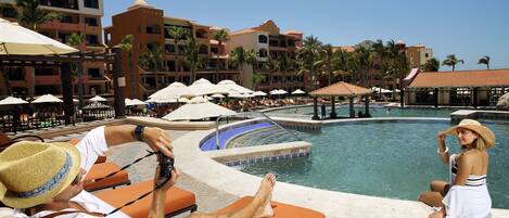Zona de piscina en un resort con sillones de descanso, sombrillas y un cielo azul brillante.