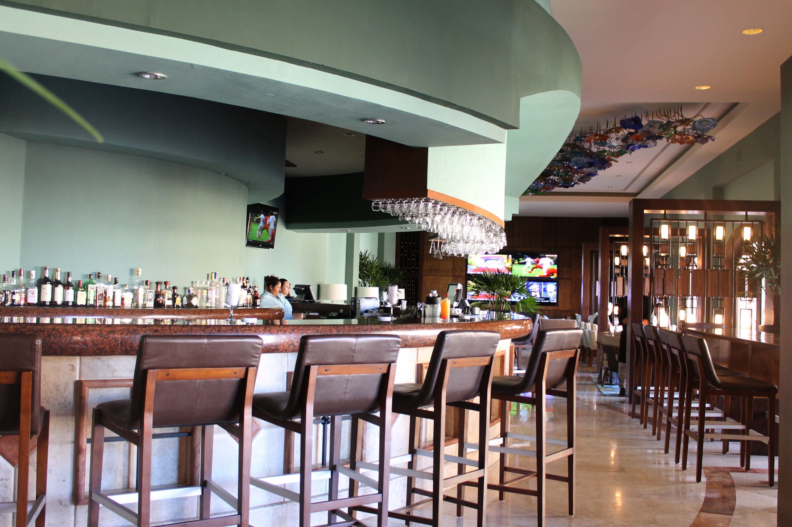A bar area with a long counter, multiple bar stools, and a television screen.