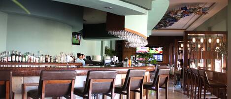 A bar area with a long counter, multiple bar stools, and a television screen.