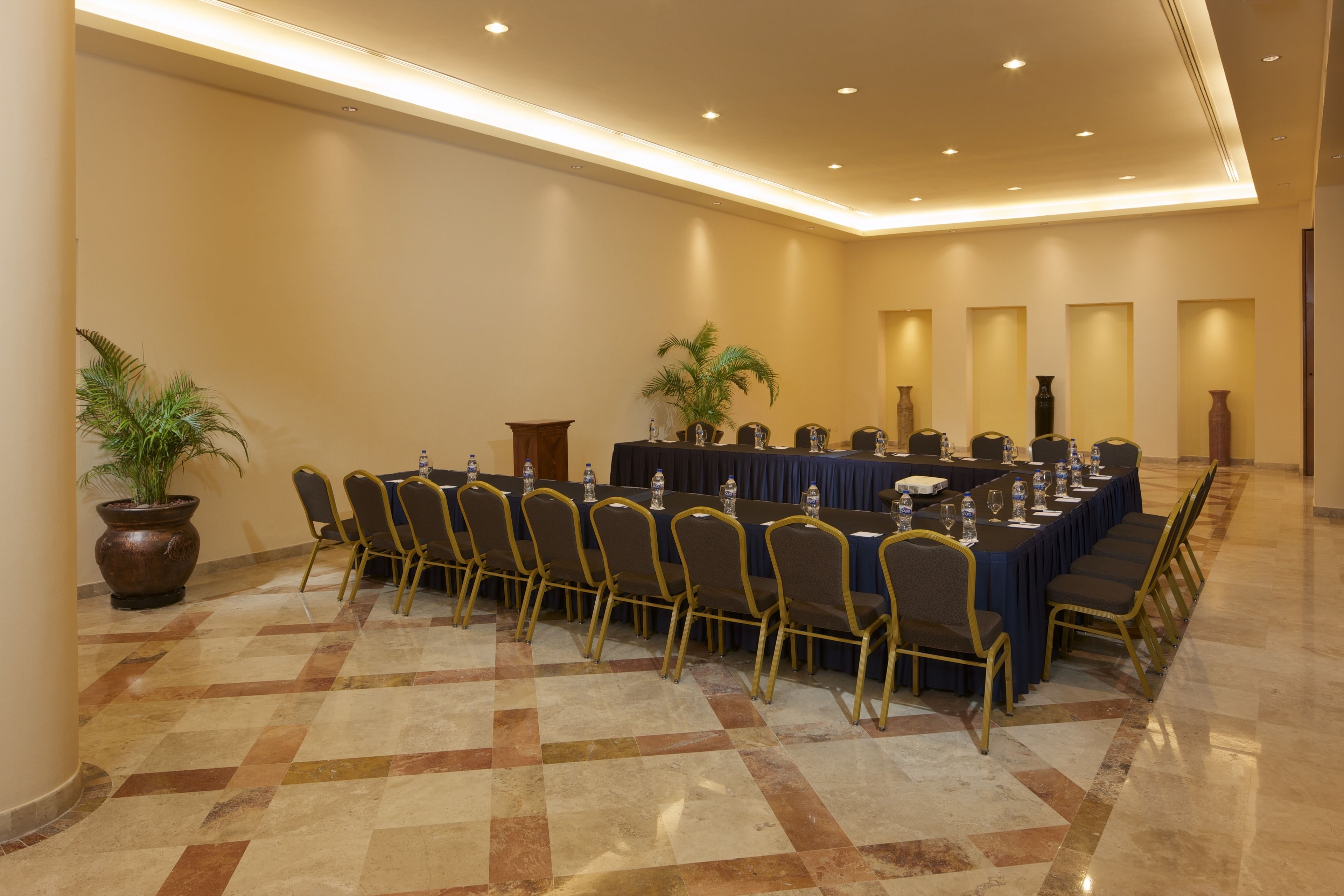 Un salón de conferencias con una larga mesa, sillas y botellas de agua.