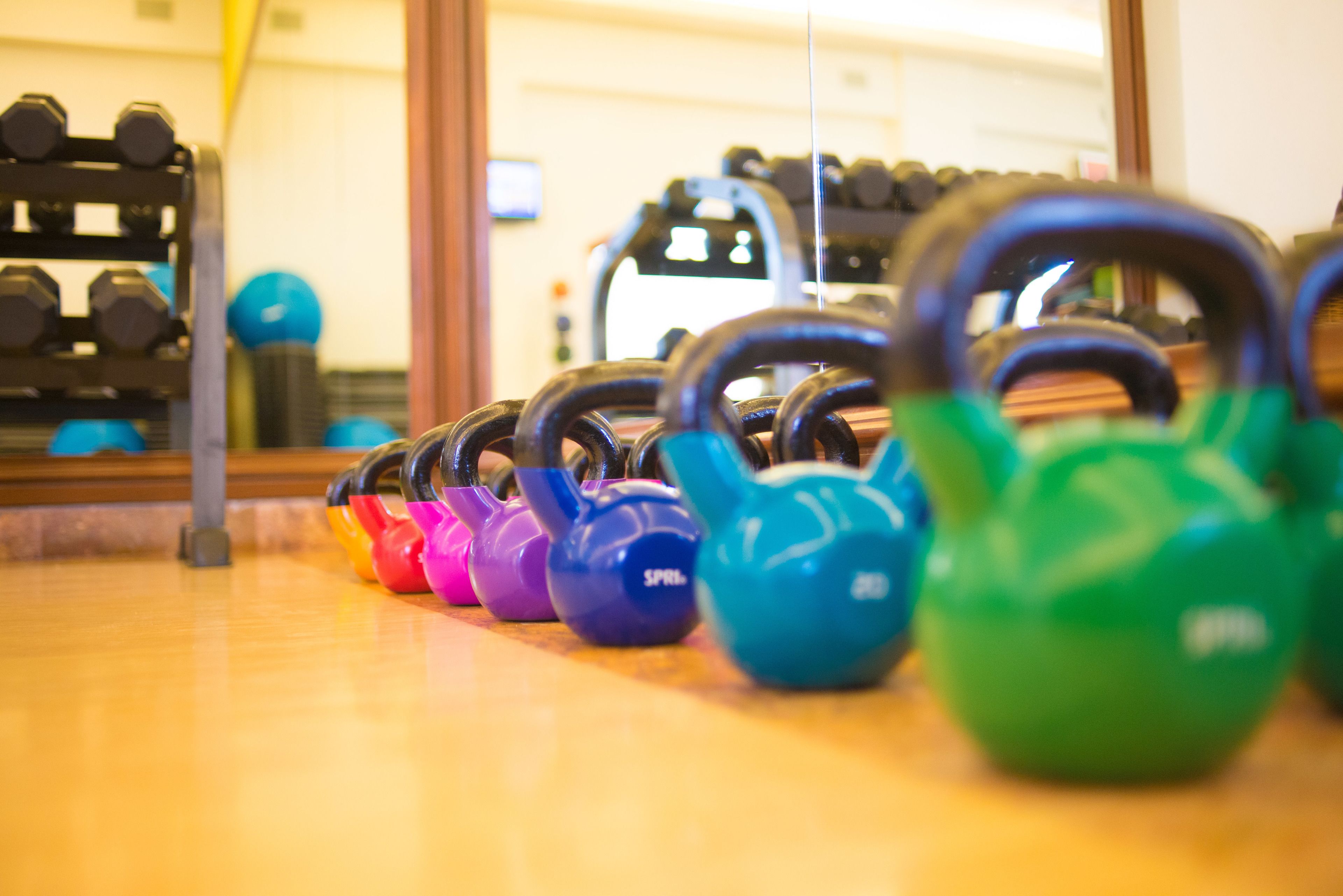 Eine Reihe Kettlebells in verschiedenen Farben auf einem Holzboden.
