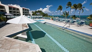 A pool area with lounge chairs and umbrellas, a clear blue sky, and palm trees. - Club St. Croix Beach & Tennis Resort by Antilles Resorts (Christiansted)