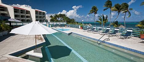 A pool area with lounge chairs and umbrellas, a clear blue sky, and palm trees.