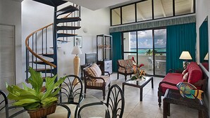 A spacious living room with a spiral staircase, comfortable seating, a coffee table, and a view of the ocean through large windows. - Club St. Croix Beach & Tennis Resort by Antilles Resorts (Christiansted)