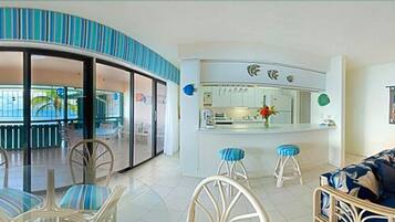 A modern living room with a curved glass wall, a kitchen with a bar area, and a dining area with chairs and a sofa.