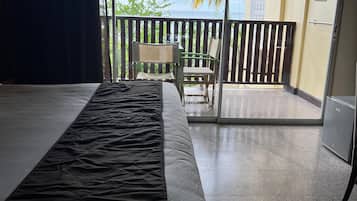 Quarto de hotel com cama, uma cadeira e varanda com vista para palmeiras e um edifício.
