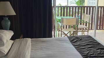 A hotel room with a bed, a lamp, a view of the sea, and a balcony with chairs.