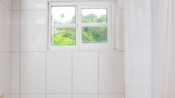 Een badkamer met witte tegels, een raam met uitzicht op groen en een bad.