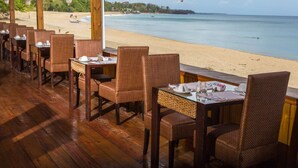 An outdoor dining area with wicker chairs and tables, overlooking a beach and ocean. - Starfish Tobago Resort (Plymouth)