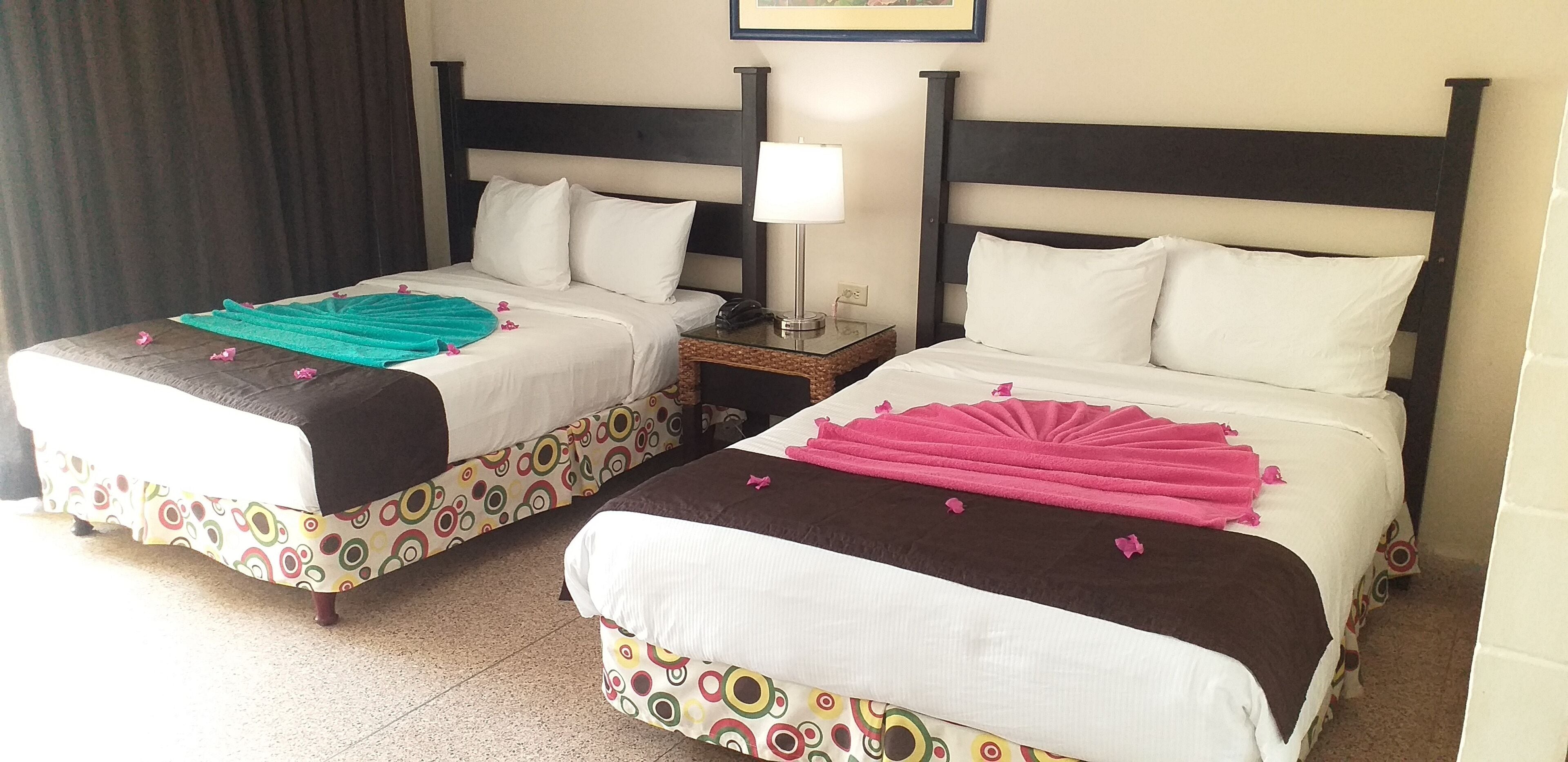 Two double beds with matching headboards and footboards, a bedside table with a lamp, and a wall-mounted phone.