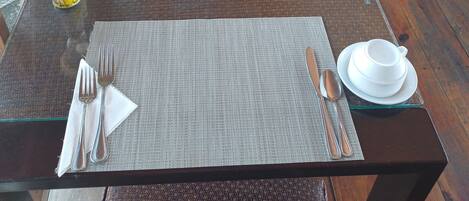 A dining area with tables set for two, featuring woven chairs and a wooden deck.