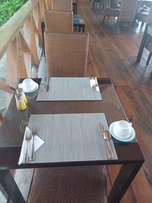 A dining area with tables set for two, featuring woven chairs and a wooden deck.
