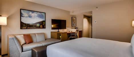 A hotel room with a large bed, a sofa, a desk, and a TV.