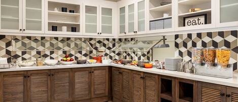 Una cocina moderna con armarios blancos, un salpicadero geométrico y una barra de desayuno con diversas opciones de comida.