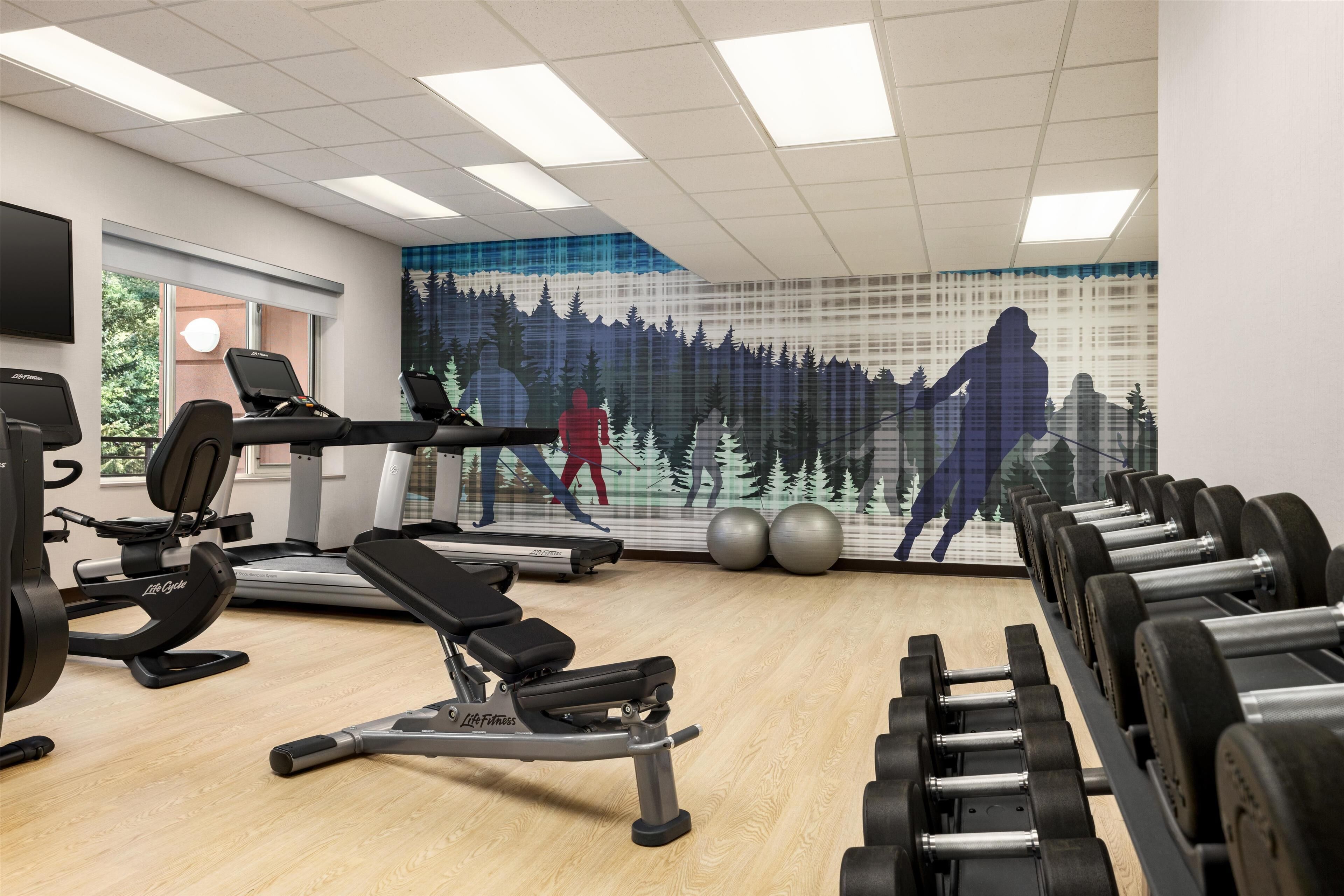 A gym with cardio equipment, weight benches, and dumbbells.