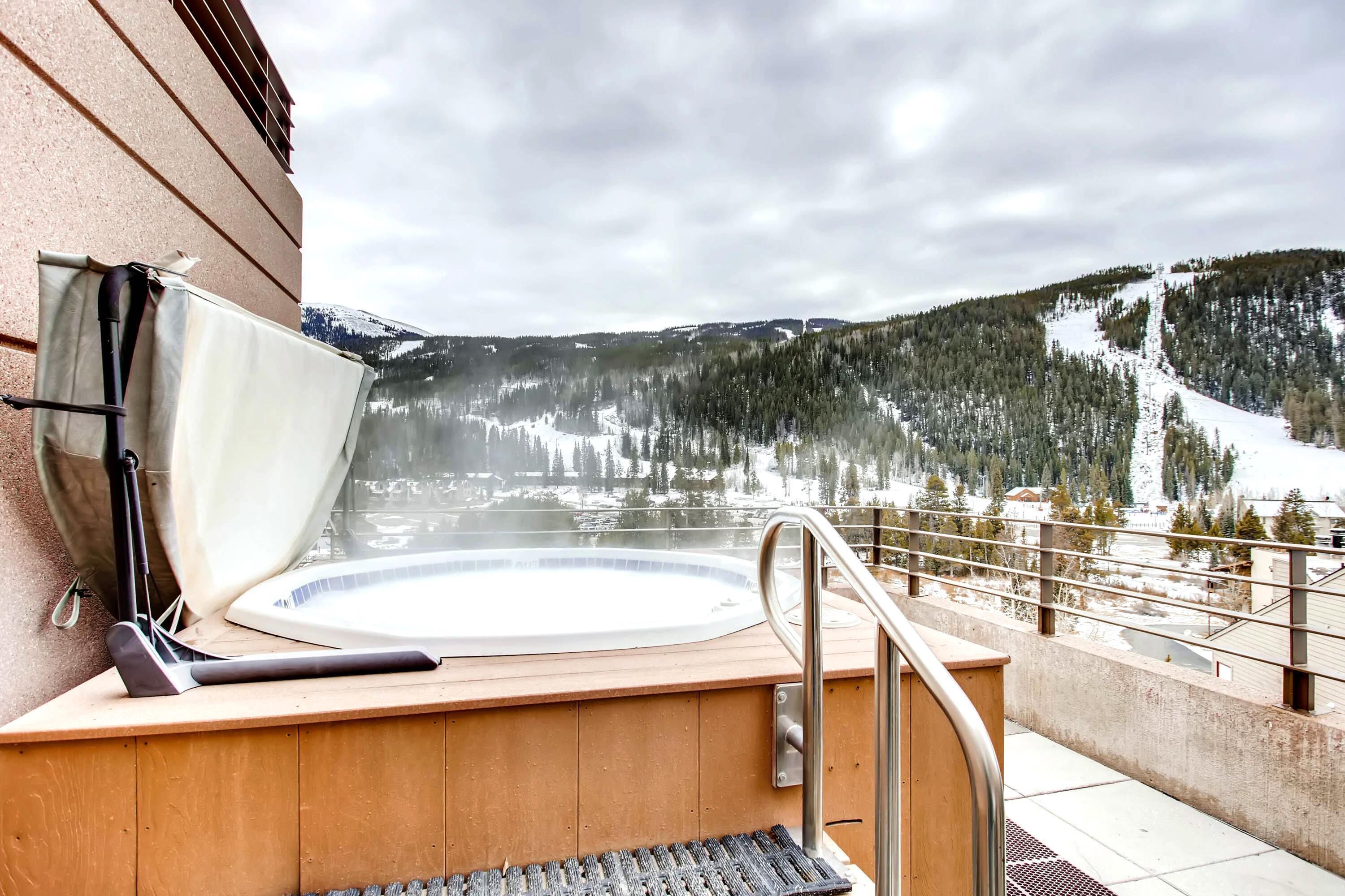 A hot tub on a wooden deck with a view of a snowy mountain and forest.