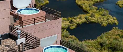 A hotel with two outdoor hot tubs on a balcony, surrounded by a natural landscape with a river and greenery.