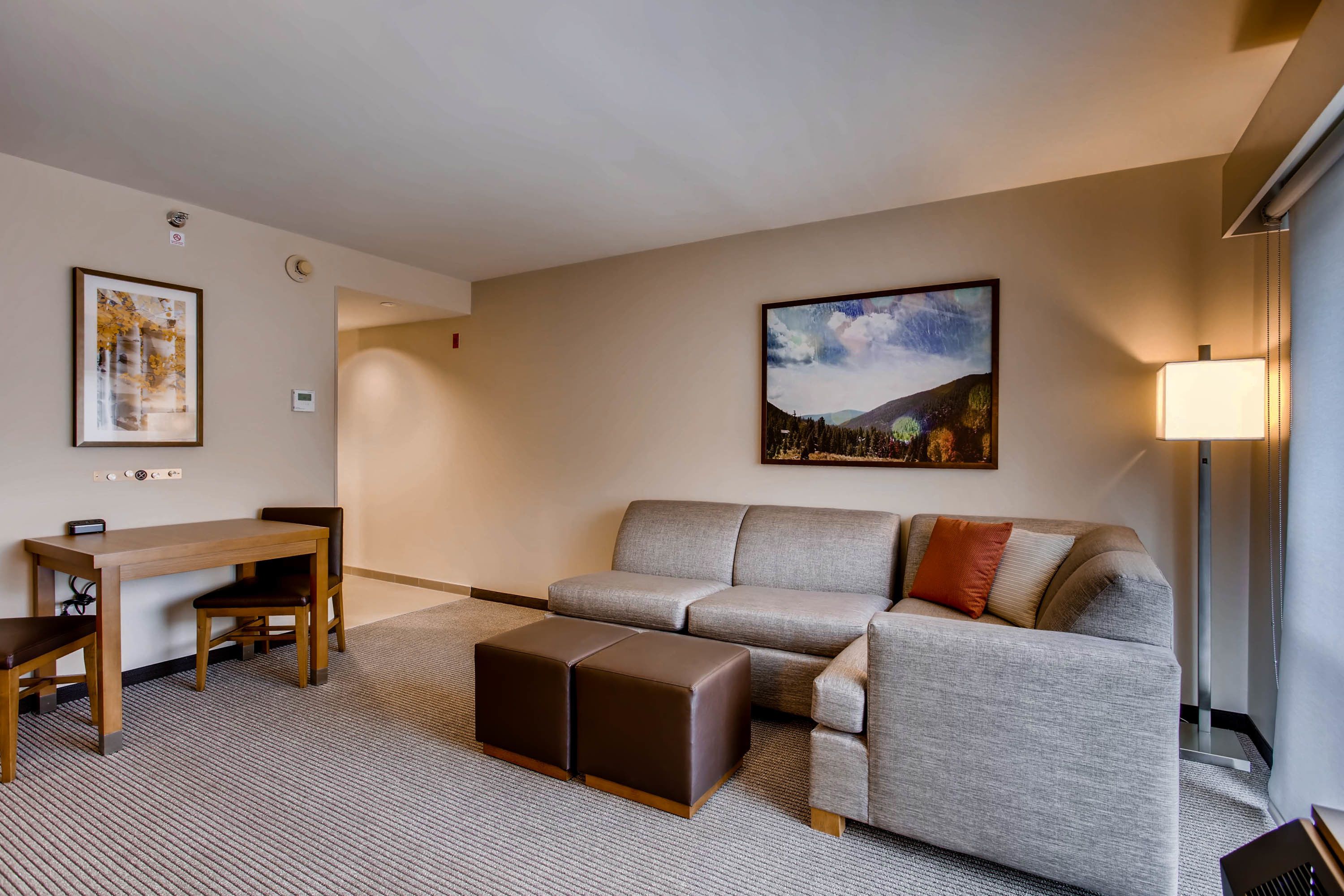 A modern hotel room with a grey sofa, a wooden table, and a lamp.