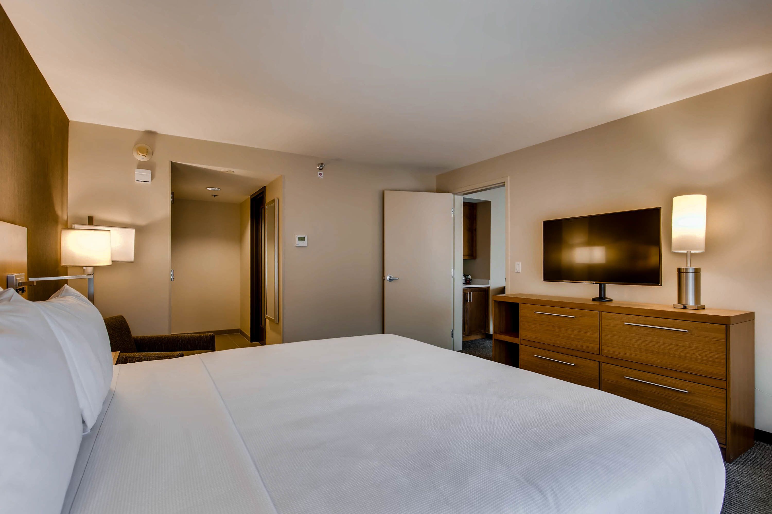 A hotel room with a large bed, a TV, a wooden dresser, and a desk with a lamp.