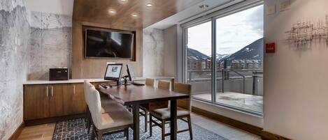 A modern dining area with a large table, chairs, and a TV mounted on the wall.