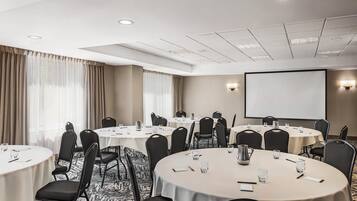 A conference room with multiple round tables, black chairs, and a projector screen.