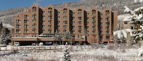 A multi-story hotel with a symmetrical facade, large windows, and a parking area in front.