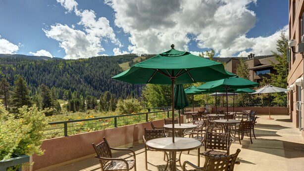 Un patio al aire libre con mesas y sillas, sombrillas verdes y una vista panorámica de la montaña.