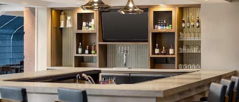 A modern bar area with a large island, bar stools, and shelves stocked with bottles and glasses.