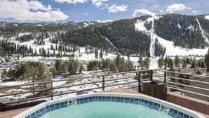 Un jacuzzi con vistas a un paisaje nevado de montaña, con zona de piscina y un edificio en primer plano.