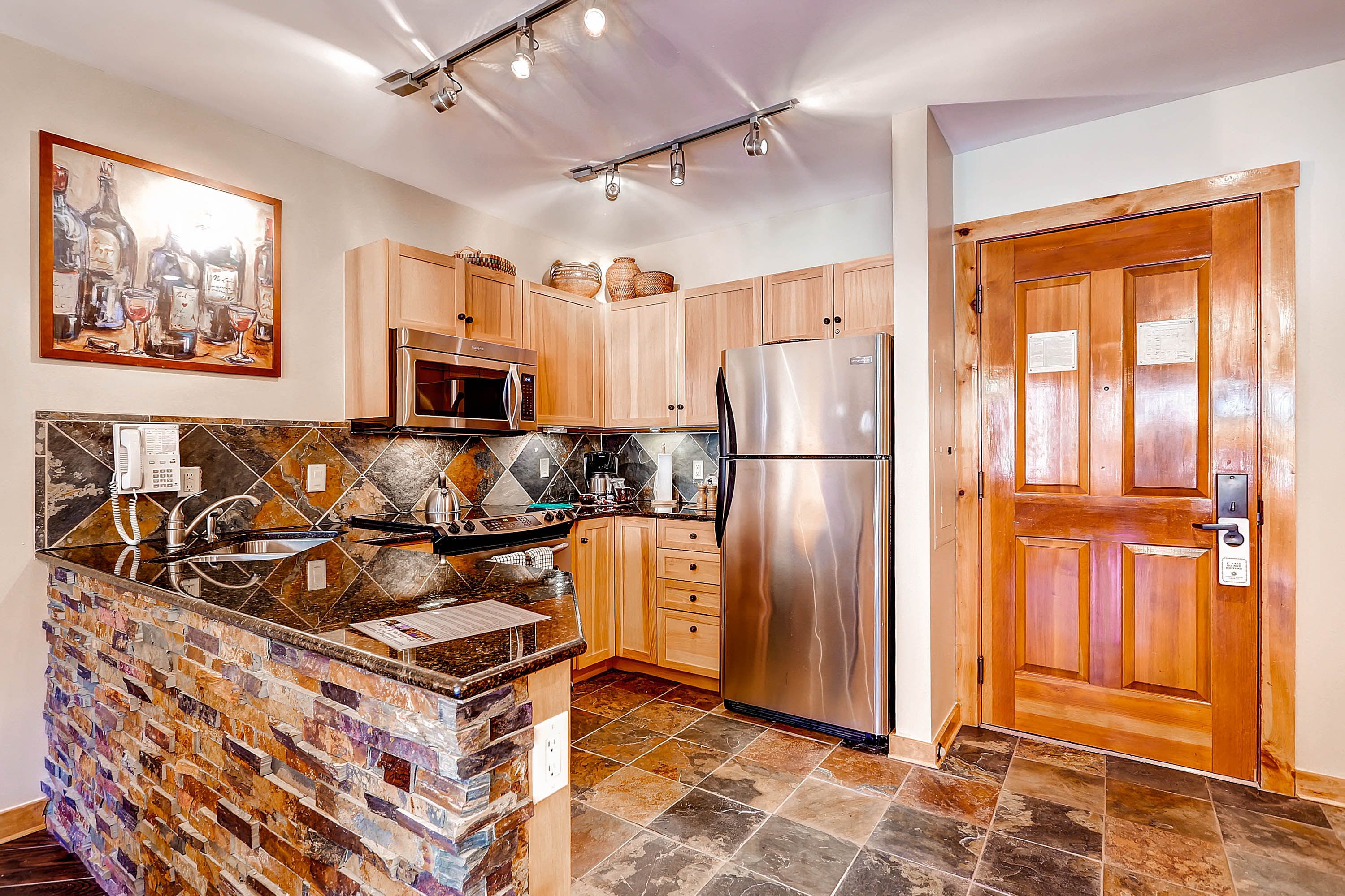 A kitchen with a stone island, stainless steel appliances, wooden cabinets, and a tiled backsplash.