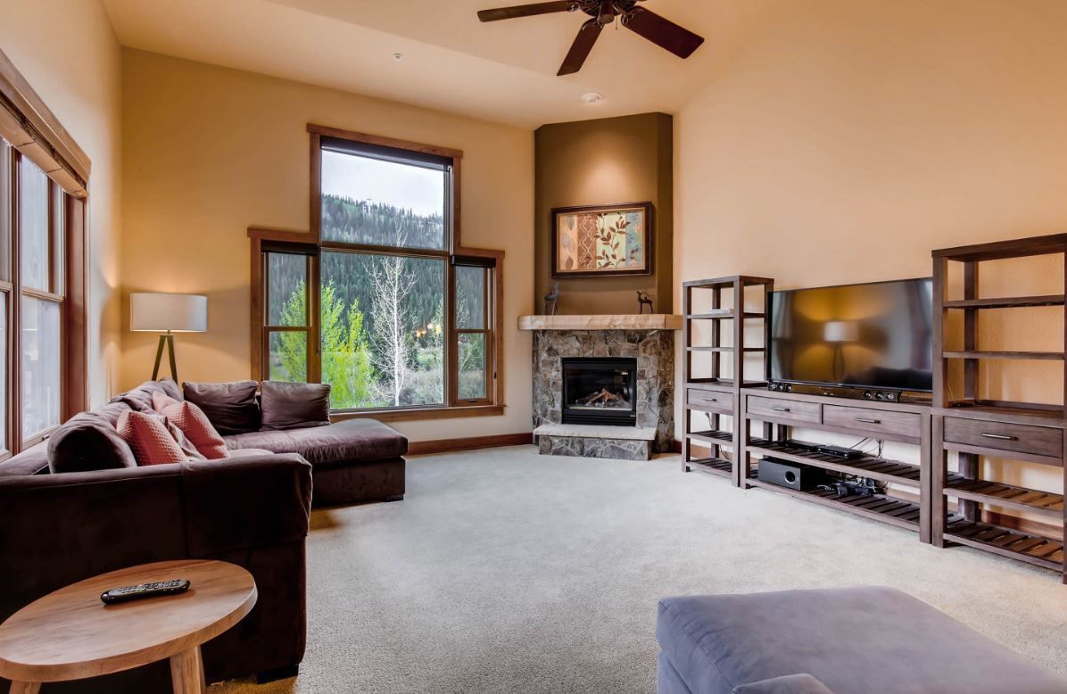 A spacious living room with a fireplace, a large TV, and a ceiling fan.