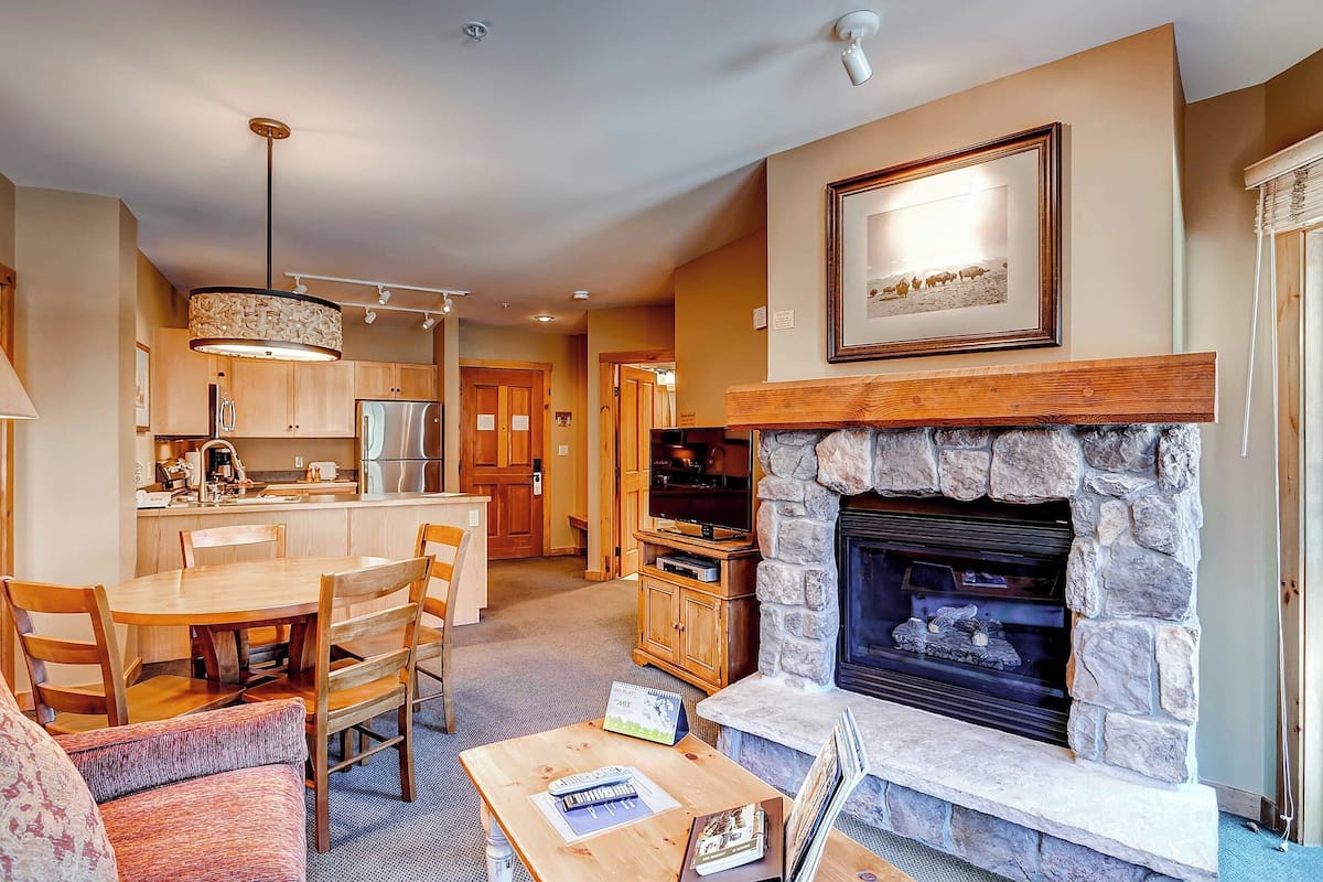 A living room with a fireplace, a dining area with wooden furniture, and a kitchen with modern appliances.