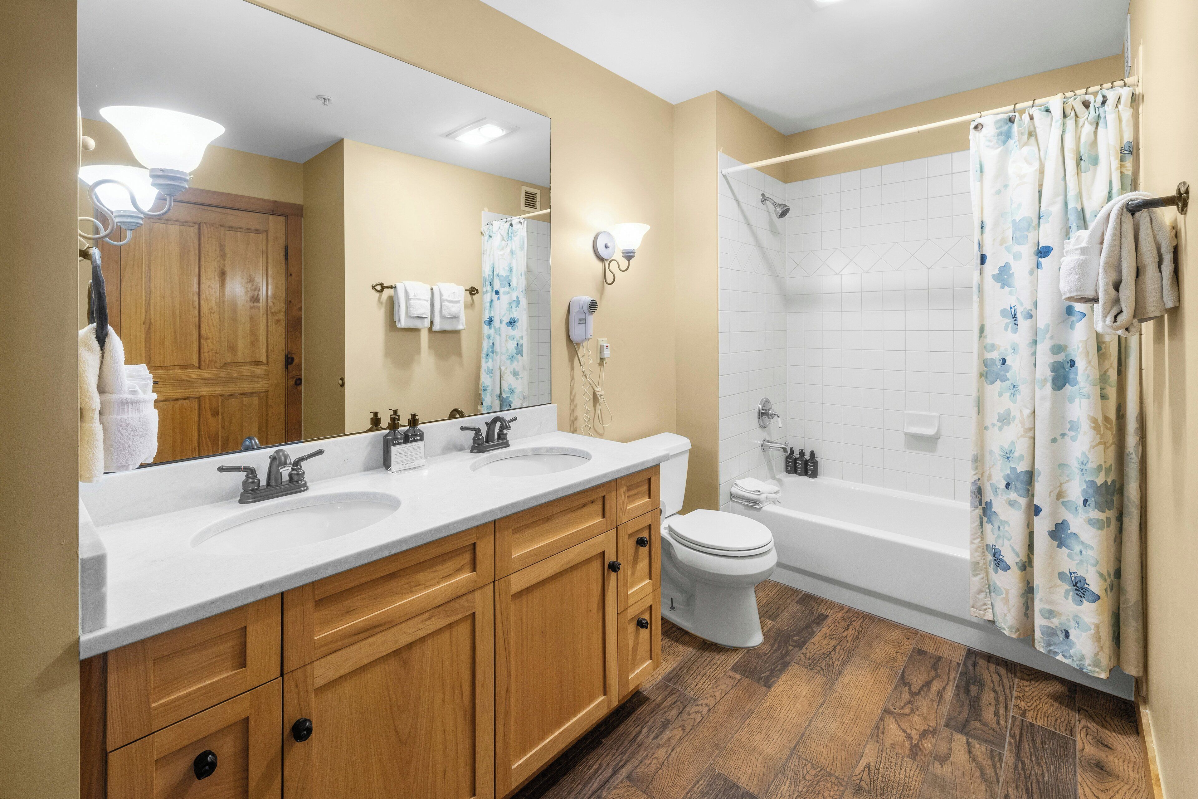 A bathroom with a double sink vanity, a toilet, a bathtub, and a shower curtain.