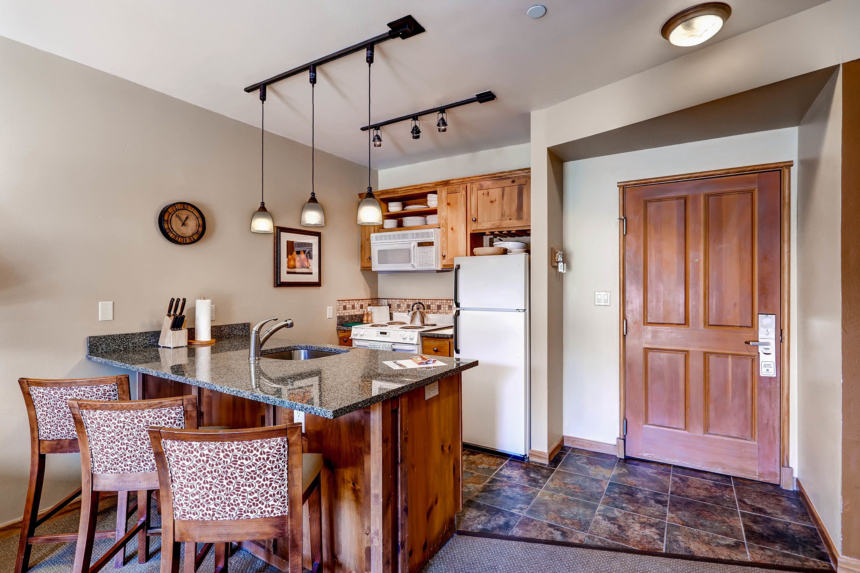 A kitchen with a central island, wooden cabinets, a microwave, and a refrigerator.