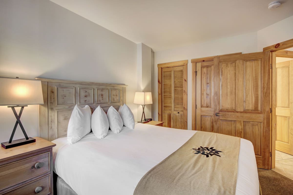 A hotel room with a large bed, two bedside lamps, a wooden headboard, and a wooden wardrobe.