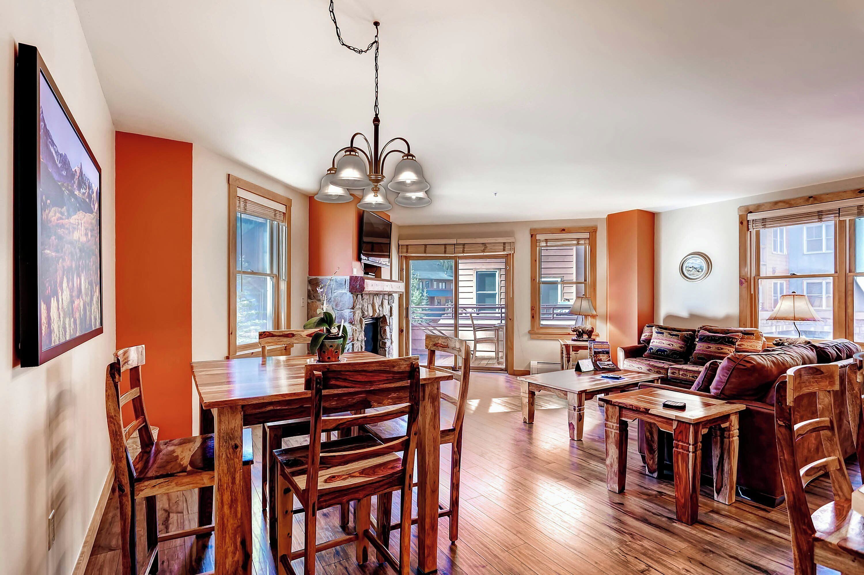 A spacious living area with a wooden dining table, chairs, a sofa, and a chandelier.