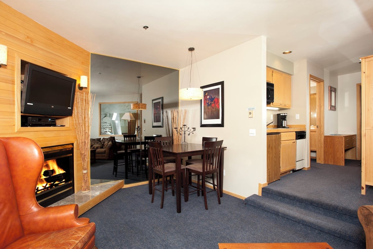 A modern living room with a fireplace, a dining area, and a kitchen.
