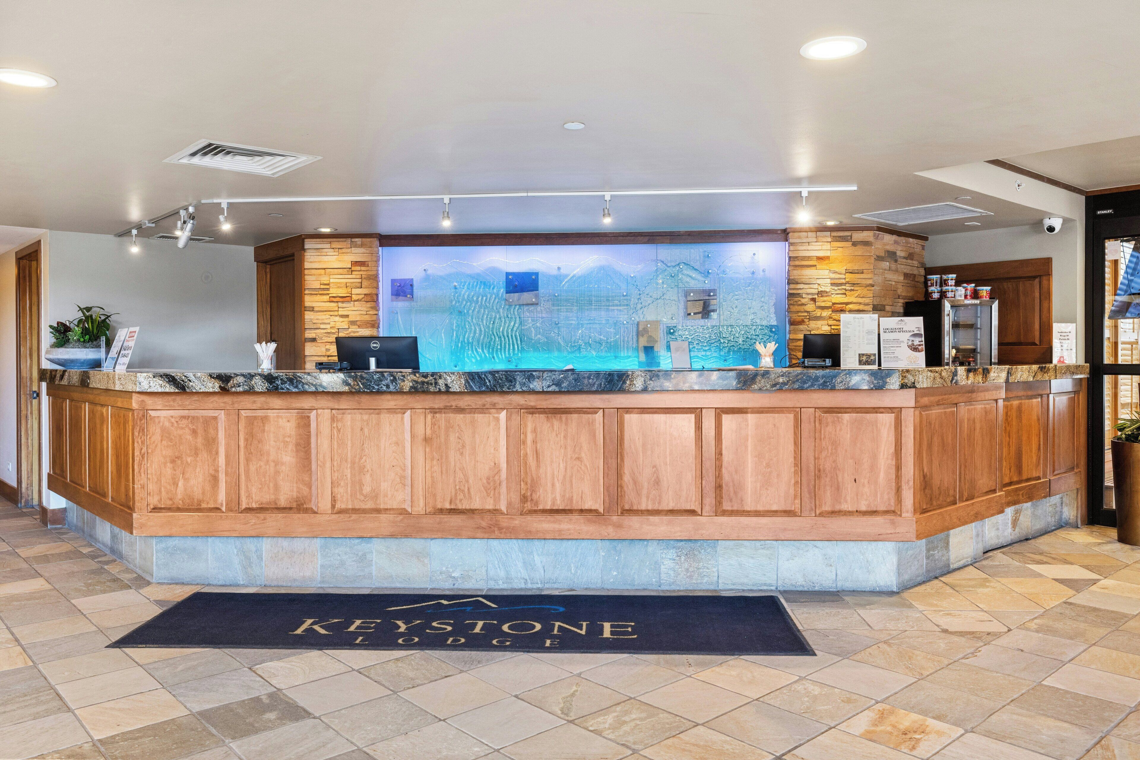 A reception desk with a stone facade, a digital screen, and a black mat with 'Keystone Lodge' text.